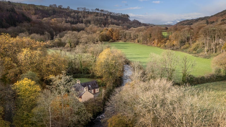 An aerial view of Abermydyr in autumn, on the edge of the Afon Aeron (River Aeron) in a wooded valley, Ceredigion